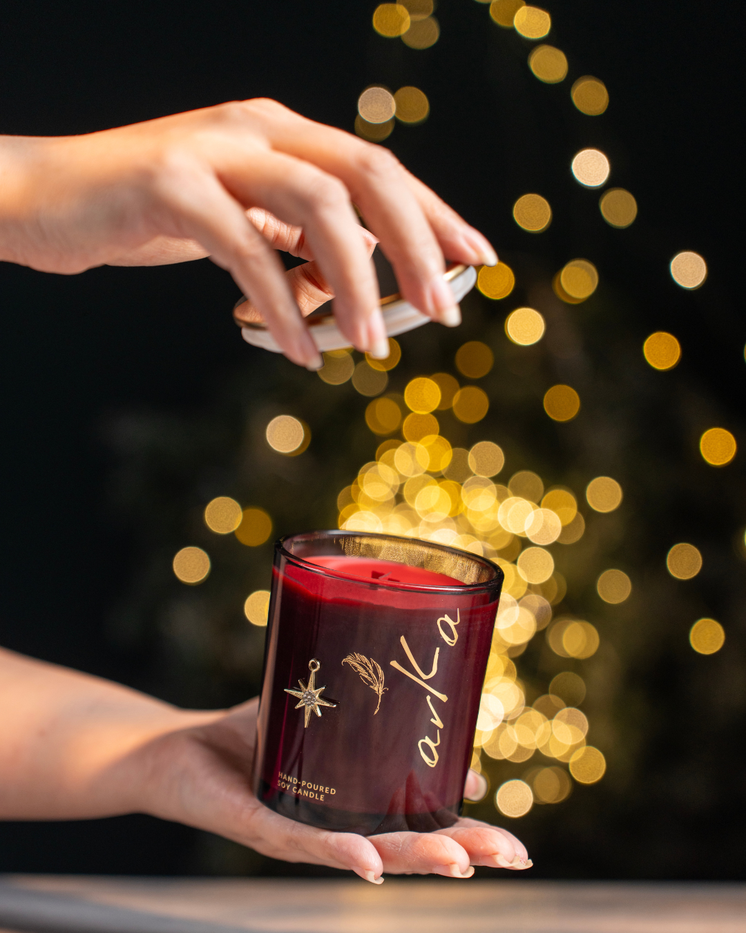 Person holding a red candle with 'arka' branding against a bokeh lights festive background
